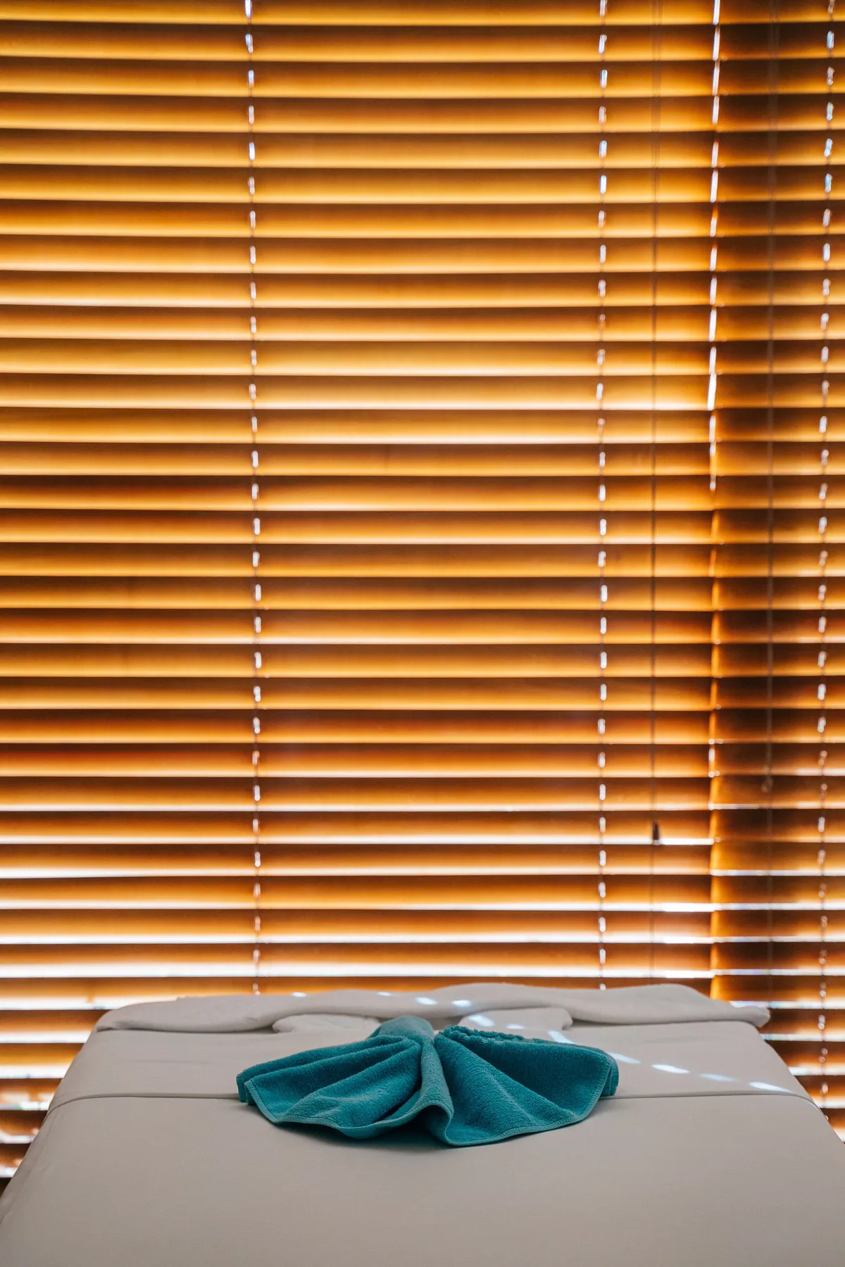 Massage table prepared with a folded towel in front of softly lit wooden blinds