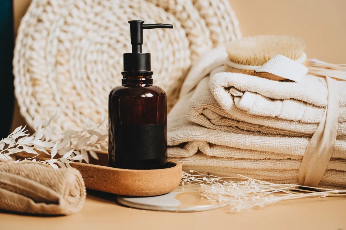 Amber pump bottle of massage oil beside stacked neutral towels